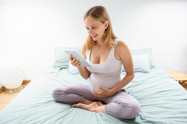 Happy expectant mom reading on tablet screen