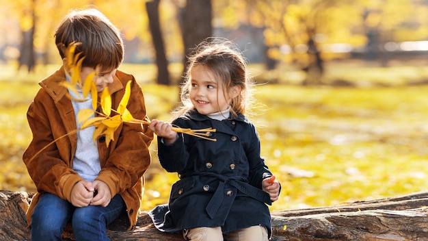 Happy family in an autumn park Brother and sister sitting on a tree trunk playing