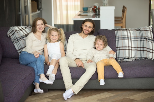 Free photo happy family of four sitting on sofa looking at camera