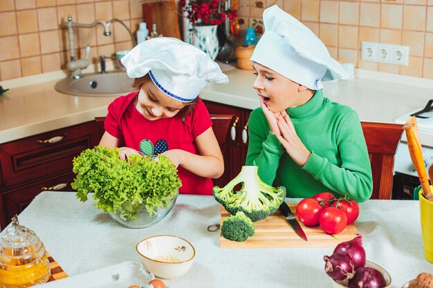 Happy family funny kids are preparing the a fresh vegetable salad in the kitchen