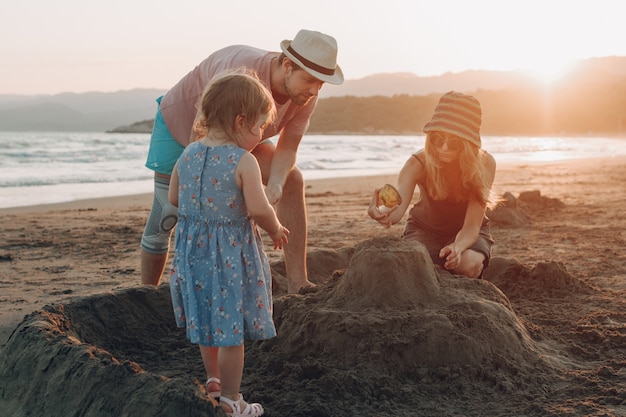 Free Photo happy family having fun together on the beach at sunset. building sand castle 