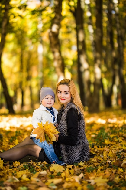 Happy family mother playing with child in autumn park near tree lying on yellow leaves. Autumn concept.