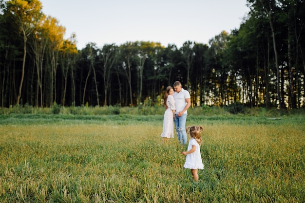 Happy family in a park in summer autumn. Mother, father and baby play in nature in the rays of sunset