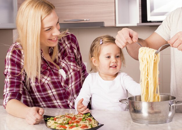 Happy family and their little daughter preparing homemade spaghetti on the kitchen counter