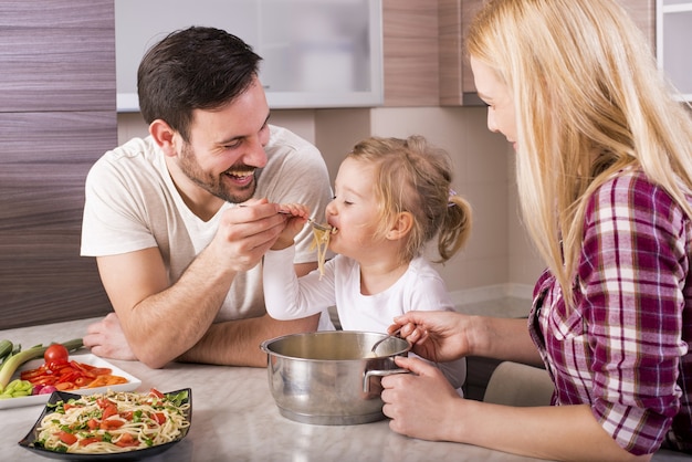 Happy family and their young daughter eating spaghetti on the kitchen counter