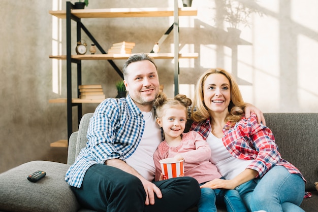 Free photo happy family watching television with daughter eating pop corn on sofa at home