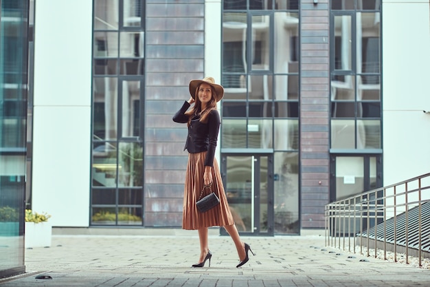 Free photo happy fashion elegant woman wearing a black jacket, brown hat and skirt with a handbag clutch walking on a european city center.