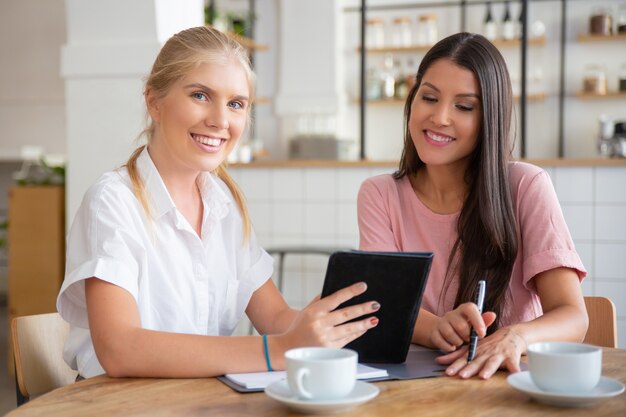 Happy female agent and customer meeting over cup of coffee, using tablet together, 