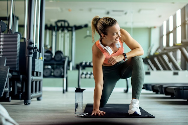 Happy female athlete doing relaxation exercises while warming up n a gym