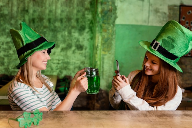 Free photo happy female friends celebrating st. patrick's day together at the bar with drink