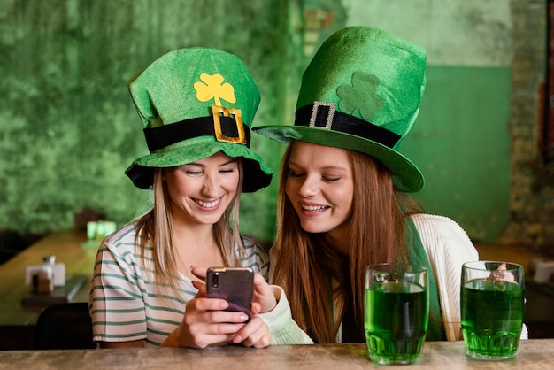 Happy female friends celebrating st. patrick's day together with smartphone at the bar