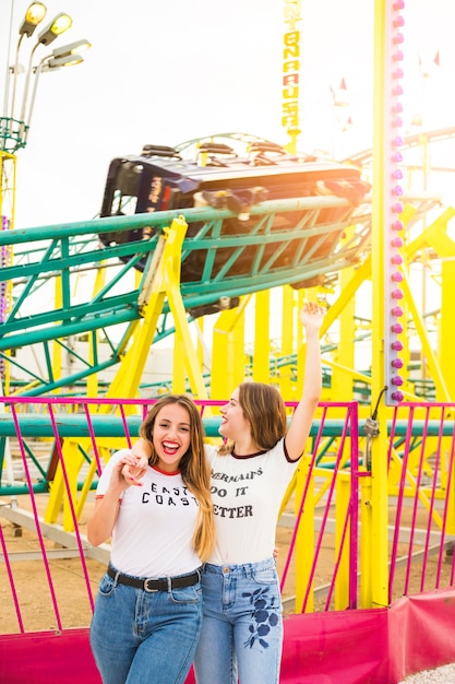 Happy female friends hanging out together in front of roller coaster ride