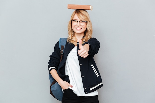 Free photo happy female nerd in funny eyeglasses with book on head showing thumb up