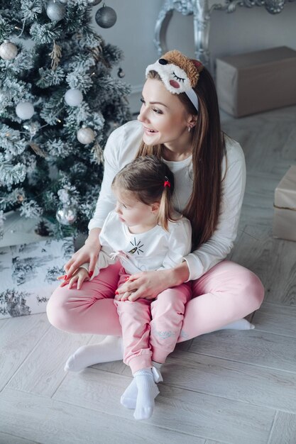 Happy festive mother and daughter hugging sitting together at decorating beautiful christmas tree