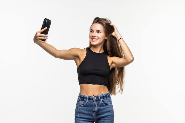 Happy flirting young girl taking pictures of herself through phone, on white