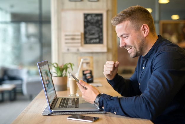 Free photo happy freelancer with tablet and laptop computer in coffee shop