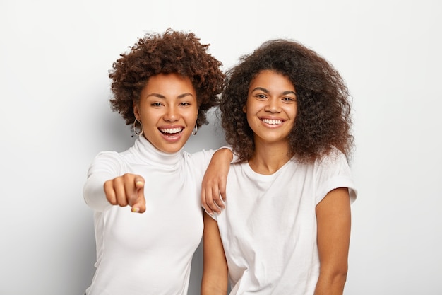 Happy friendly two millennial girls have glad faces, stand next to each other, point into distance