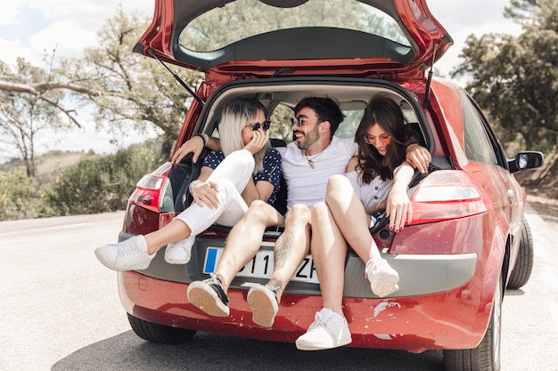 Happy friends making fun in the car trunk on road