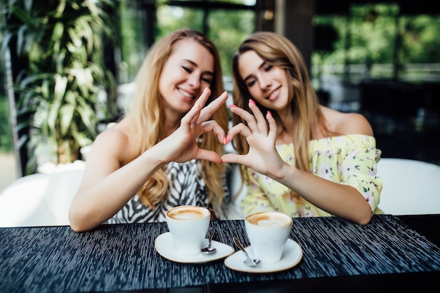 Free Photo happy friends making heart gesture and drinking coffee at the terrace