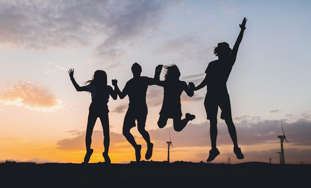 Happy friends silhouettes jumping on sunset