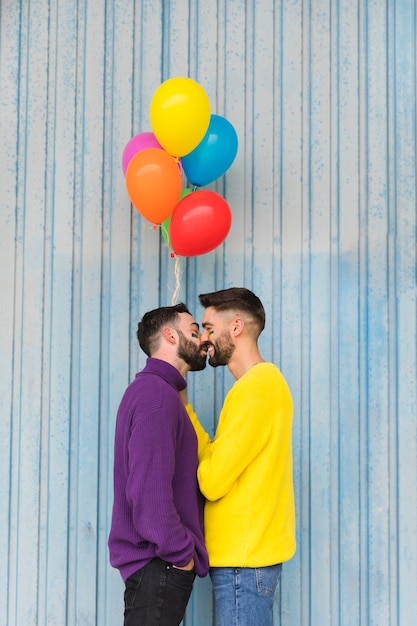 Happy gay sweethearts kissing and holding balloons