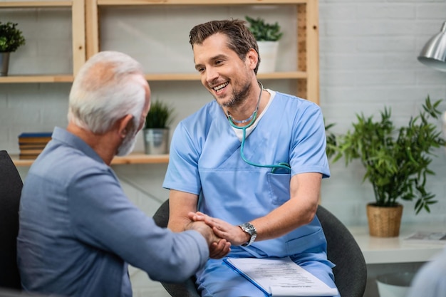 Happy general practitioner talking to senior man while shaking hands with him during a home visit