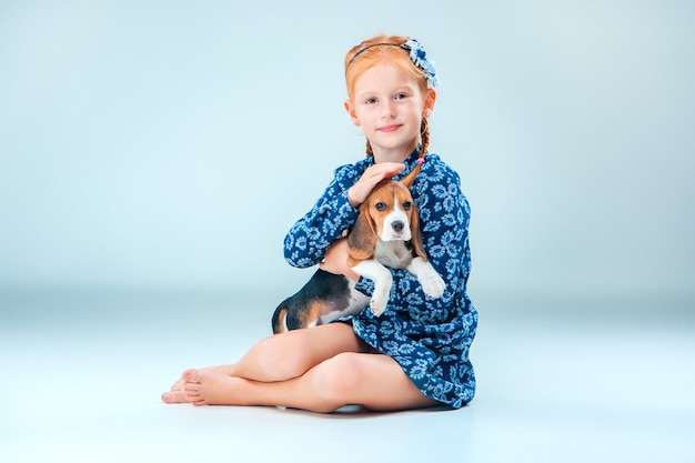 The happy girl and a beagle puppy on gray wall