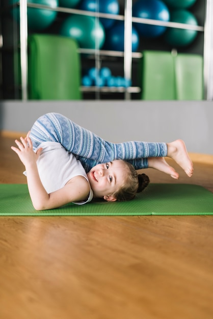 Happy girl child practicing yoga on mat looking at camera