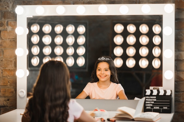 Free photo happy girl looking at her reflection in mirror at backstage