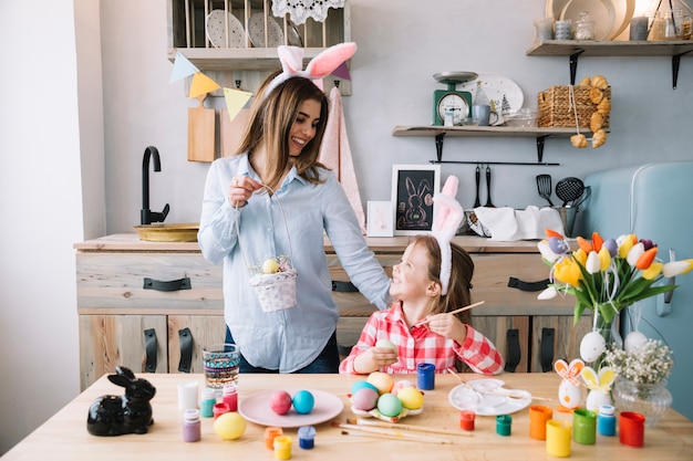 Free Photo happy girl painting eggs for easter near mother with basket 