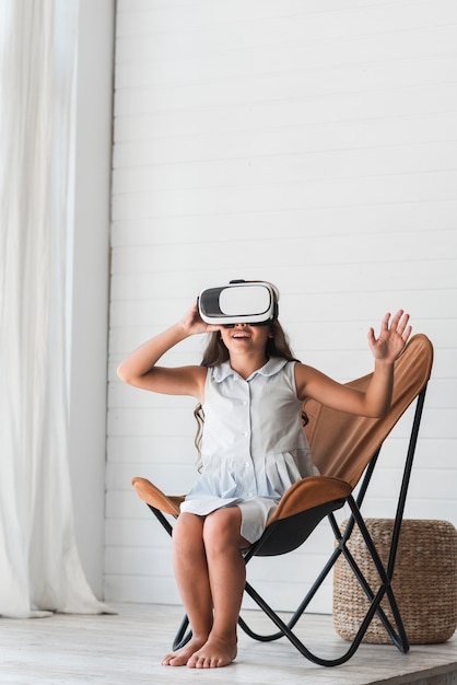 Free Photo happy girl sitting on chair wearing virtual reality glasses at home