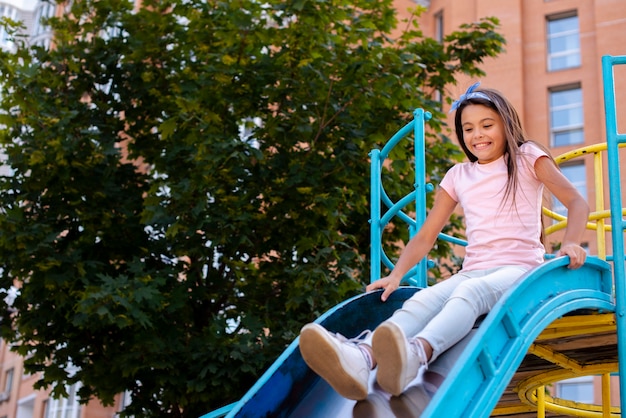 Happy girl sliding on a slide in a playground 