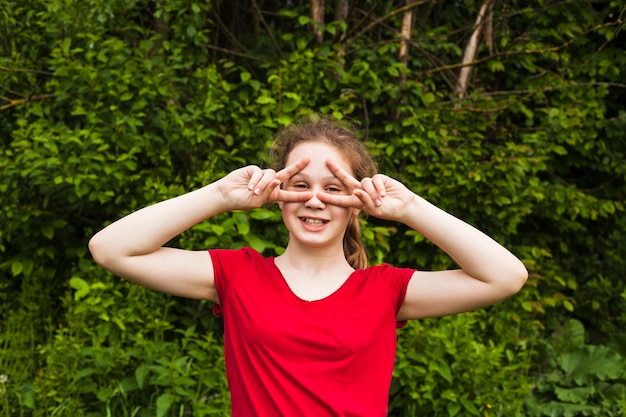 Free Photo happy girl standing in park and looking through v sign