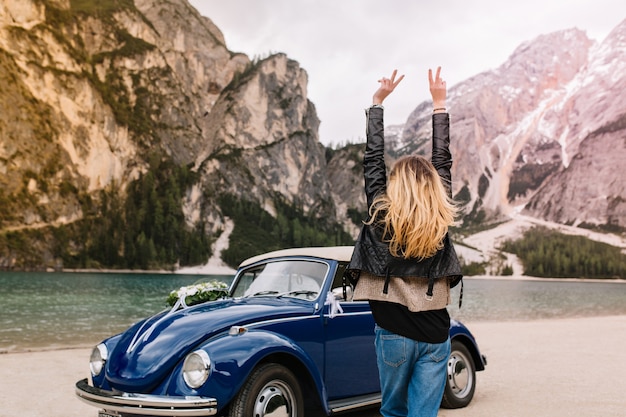 Happy girl in stylish attire having fun in Italy looking at mountains and funny dancing with hands up