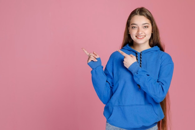 Happy girl with long fair hair pointing away with fingers showing right direction and smiling