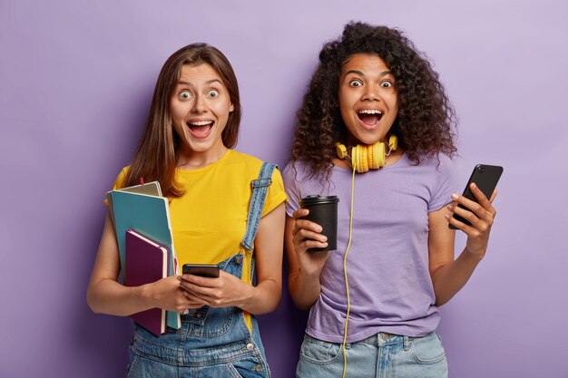 Happy girlfriends posing with their phones