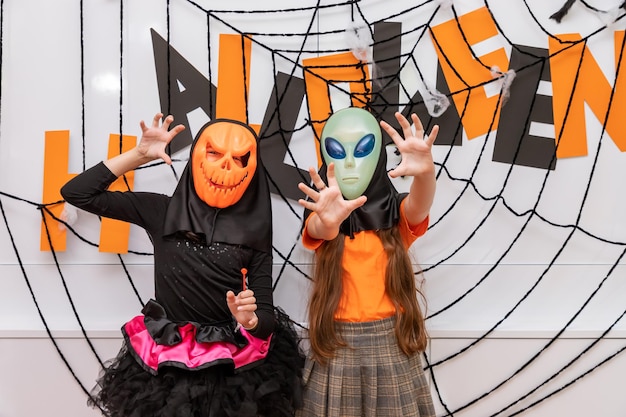 Free Photo happy girls standing front of halloween party decoration wearing pumpkin jacko'lantern and alien mask