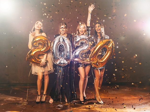 Free photo happy gorgeous girls in stylish sexy party dresses holding gold and silver 2020 balloons