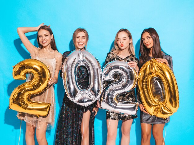 Happy Gorgeous Girls In Stylish Sexy Party Dresses Holding Gold and Silver 2020 Balloons