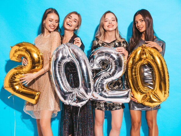 Happy Gorgeous Girls In Stylish Sexy Party Dresses Holding Gold and Silver 2020 Balloons