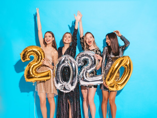 Happy Gorgeous Girls In Stylish Sexy Party Dresses Holding Gold and Silver 2020 Balloons