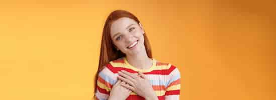 Free photo happy grateful passionate stylish redhead european girl thanking dearest friend lovely sweet gift press palms heart smiling broadly tilting head amused gratefully appreciate orange background