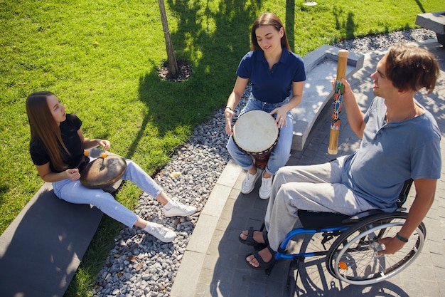 Free Photo happy handicapped man on a wheelchair spending time with friends playing live instrumental music outdoors.