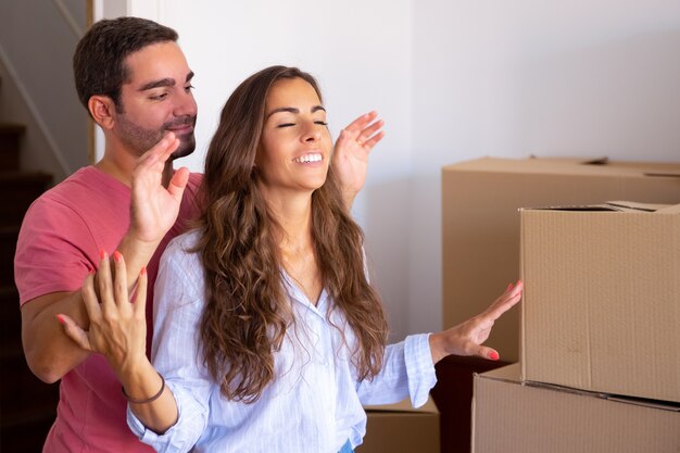 Happy handsome man leading his girlfriend with closed eyes into their new apartment with carton boxes