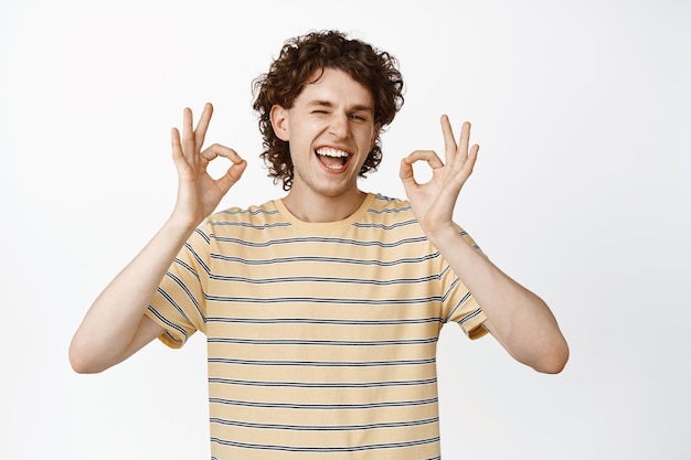 Free Photo happy handsome young man showing okay sign laughing and nod in approval standing over white background