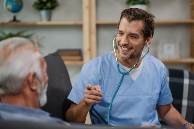 Free photo happy healthcare worker communicating with senior man and pointing at him while being in a home visit