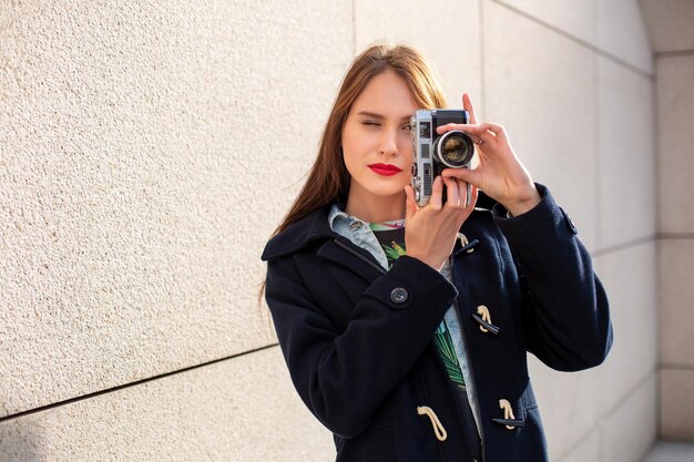 Happy hipster girl making photo with retro camera on city street. Travel concept