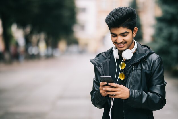 Happy indian man walking and using a smart phone to listen music with headphones