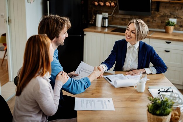 Happy insurance agent shaking hands with young couple after successful meeting