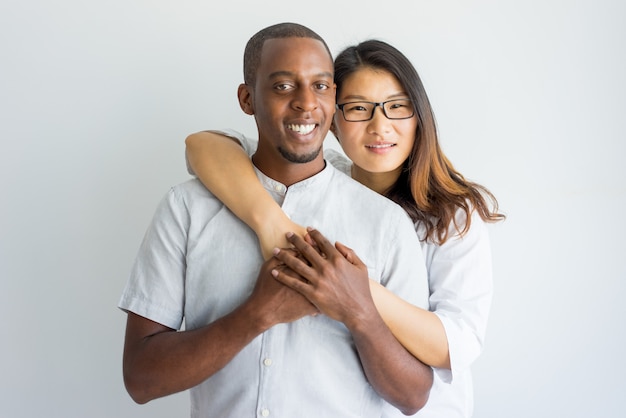 Happy interracial couple embracing and looking at camera. 